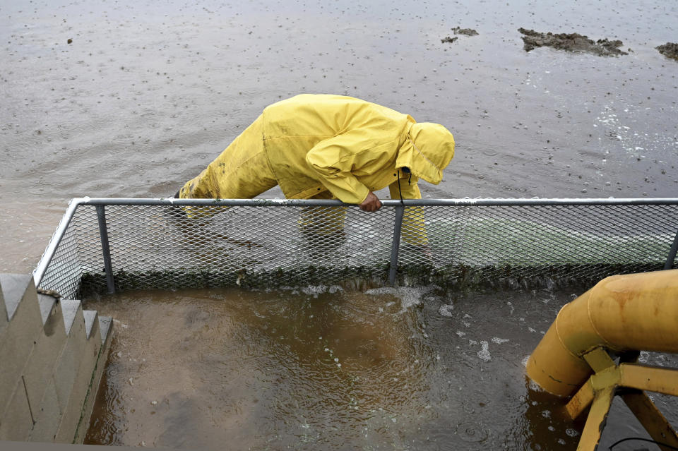 Eduardo Avilez clears debris from a grate at a water pump draining water from Southland Sod farm, Thursday, Dec. 21, 2023, in Oxnard, Calif. A Pacific storm has pounded parts of Southern California with heavy rain, street flooding and a possible tornado, adding to hassles as holiday travel gets underway. (AP Photo/Michael Owen Baker)