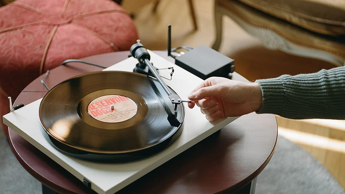  Pro-Ject Primary E1 turntable with a hand putting the needle on a vinyl. 