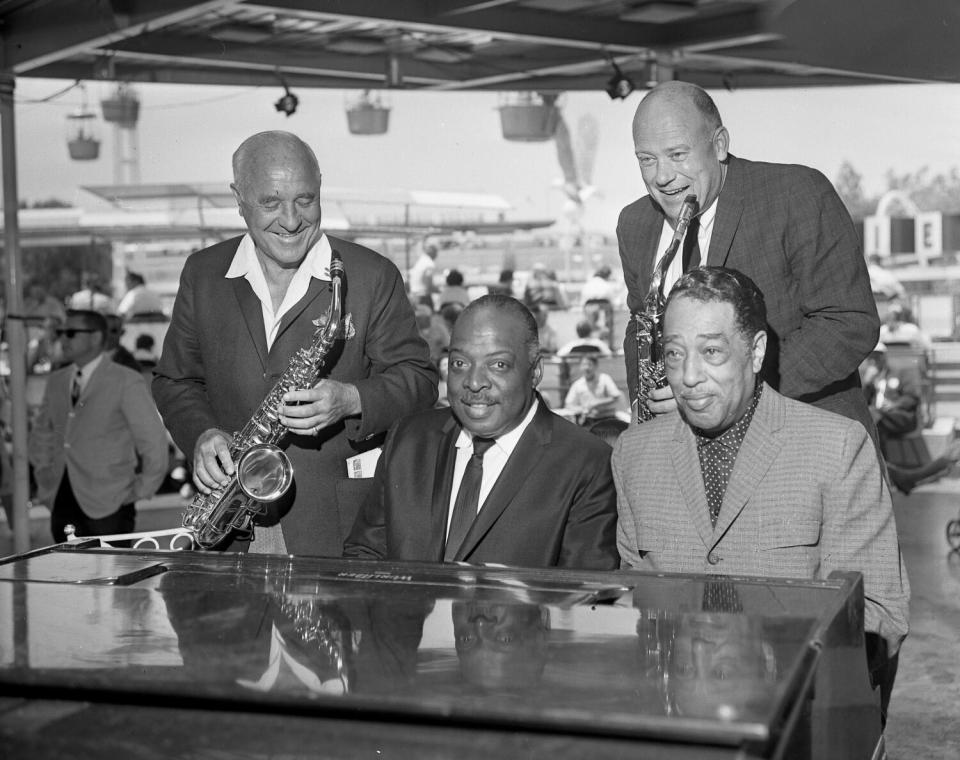 Suited musicians line up at a piano