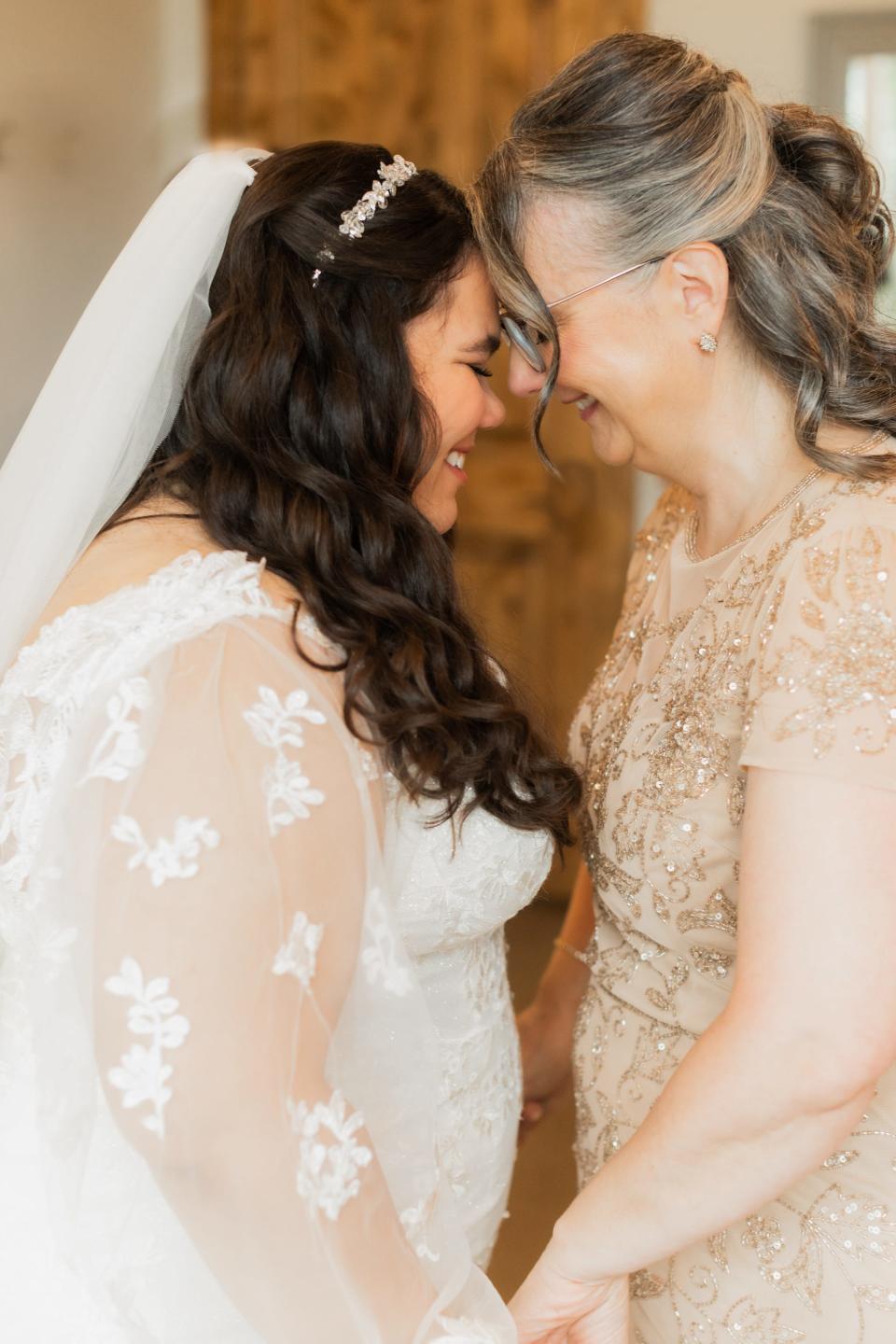 A bride and her mother lean their heads together.
