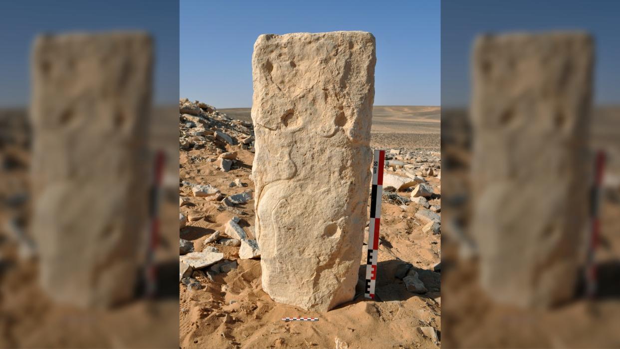  Here we see a rectangular stone standing upright with carving on it in the middle of a desert. 