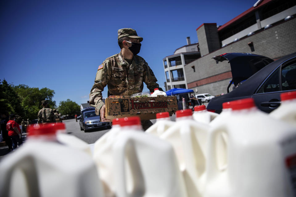 Rhode Island National Guard Pfc. Gerald Moniz distributes gallons of milk and produce along with volunteers with the Dairy Farmers of America to families in need, Wednesday, May 27, 2020, in Pawtucket, R.I. Dairy farmers have a milk surplus because demand has dropped as schools and restaurants closed during the coronavirus pandemic, and some farmers have had to pour excess milk away. Farmers donated the 4,300 gallons of milk given away today at McCoy Stadium. (AP Photo/David Goldman)