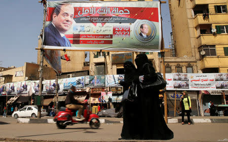 Woman wearing a full veil (niqab) walk in front of posters of Egypt's President Abdel Fattah al-Sisi during the preparations for tomorrow's presidential election in Cairo, Egypt March 25, 2018. REUTERS/Ammar Awad