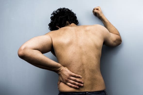 Young man with severe back pain from sciatica is banging his fist against the wall. Desaturated colors and high clarity help ill