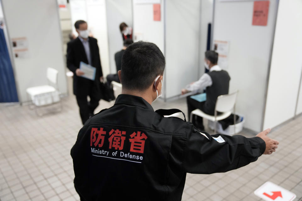 A staff member of Defense Ministry guides local residents who received the booster shot of the Moderna coronavirus vaccine at a mass vaccination center operated by Japanese Self-Defense Force Monday, Jan. 31, 2022, in Tokyo. (AP Photo/Eugene Hoshiko, Pool)