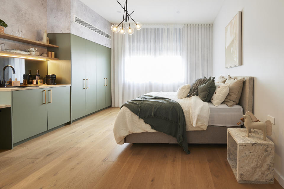 A wide shot of the bedroom with green cupboards on the left and the bed on the right. 