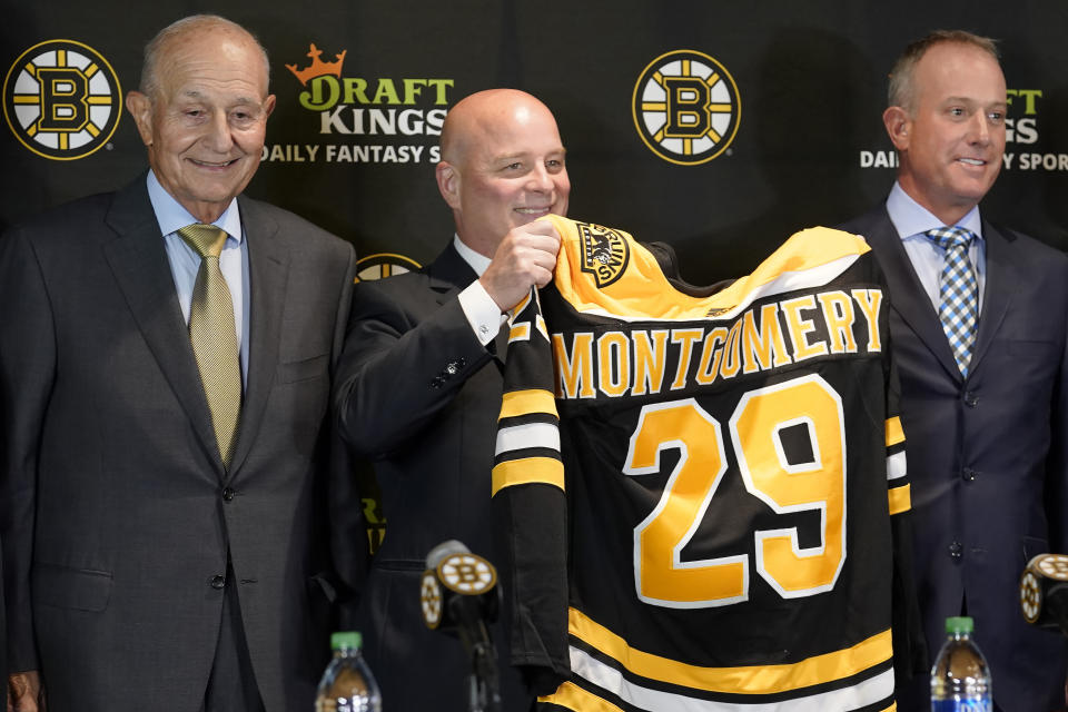 Boston Bruins newly hired head coach Jim Montgomery, center, displays a Bruins jersey while standing with team owner Jeremy Jacobs, left, and CEO Charlie Jacobs, right, during a news conference, July 11, 2022, in Boston. The NHL coaching carousel last summer involved the Boston Bruins firing coach Bruce Cassidy and the Vegas Golden Knights doing the same to Peter DeBoer. Cassidy replaced DeBoer in Vegas and DeBoer went to the Dallas Stars. Jim Montgomery had been fired by the Stars three seasons ago for inappropriate conduct but had gotten back into the NHL as an assistant in St. Louis. Montgomery then replaced Cassidy in Boston. All three teams led their respective division at the All-Star break and are on track to make the playoffs. (AP Photo/Steven Senne, file)