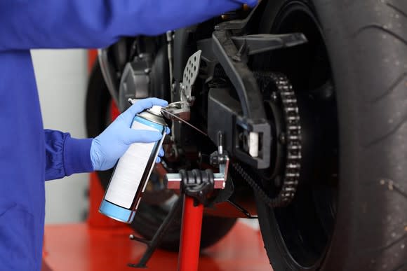 A mechanic applies lubrication to a motorbike chain.