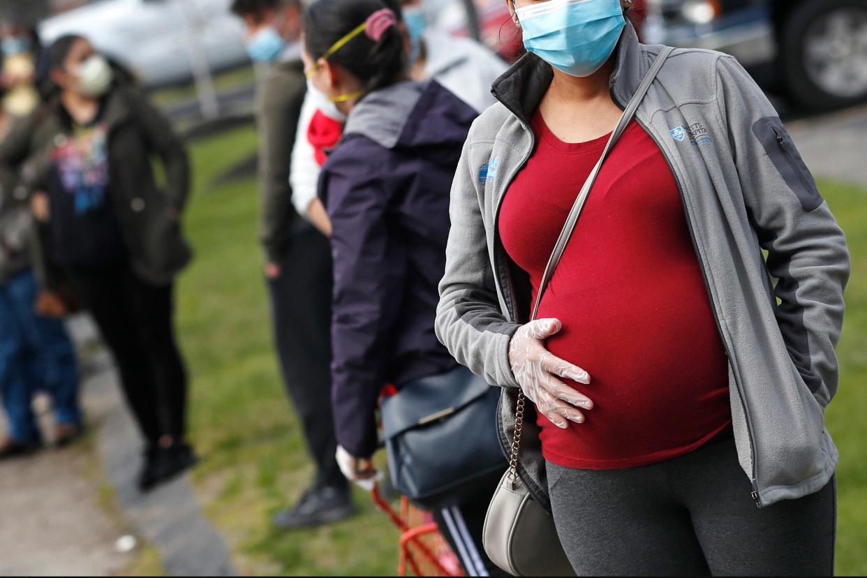 A pregnant woman in a mask and gloves waits in line for groceries during a food drive at St. Mary's Church in Waltham, Mass.