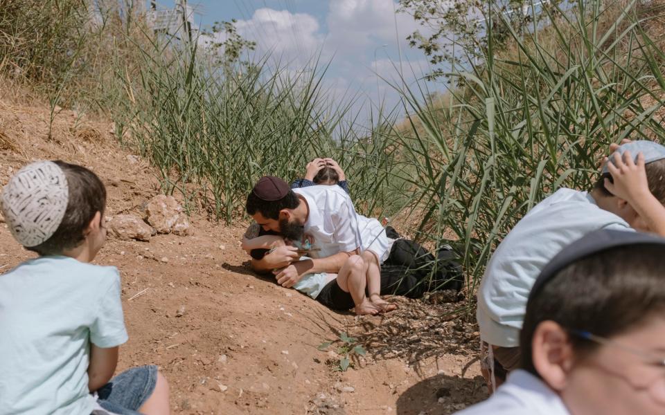Israelis take cover as a siren sounds a warning of incoming rockets fired from the Gaza Strip