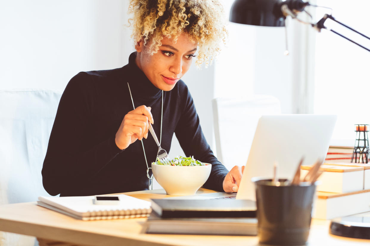 Woman eating lunch at her desk. (Getty Images)