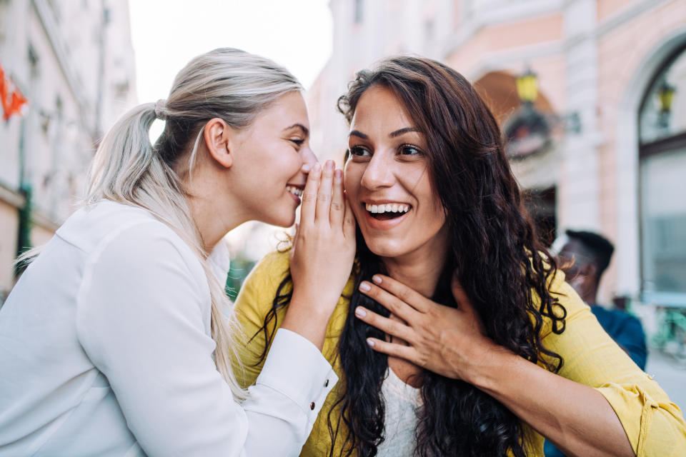Woman whispers into friend's ear and she laughs