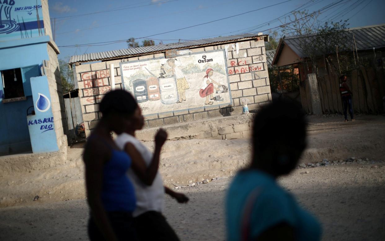 Women walk past an Oxfam sign in Corail, a camp for people displaced by the 2010 earthquake, on the outskirts of Port-au-Prince - REUTERS