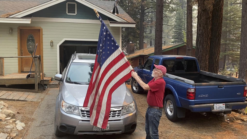 Bill Roberts rolls up an American flag in front of his house in South Lake Tahoe, Calif., on Tuesday, Aug. 31, 2021, a day after the city was ordered to evacuate because the approaching Caldor Fire. While more than 20,000 people packed roads leading out of Lake Tahoe on Monday to flee the Caldor Fire closing in on the resort community, a handful of people decided to buck the mandatory evacuation orders and stay behind. (AP Photo/Terry Chea)