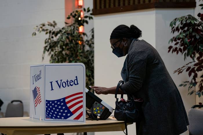 Person wearing a mask casting a ballot at an "I Voted" booth