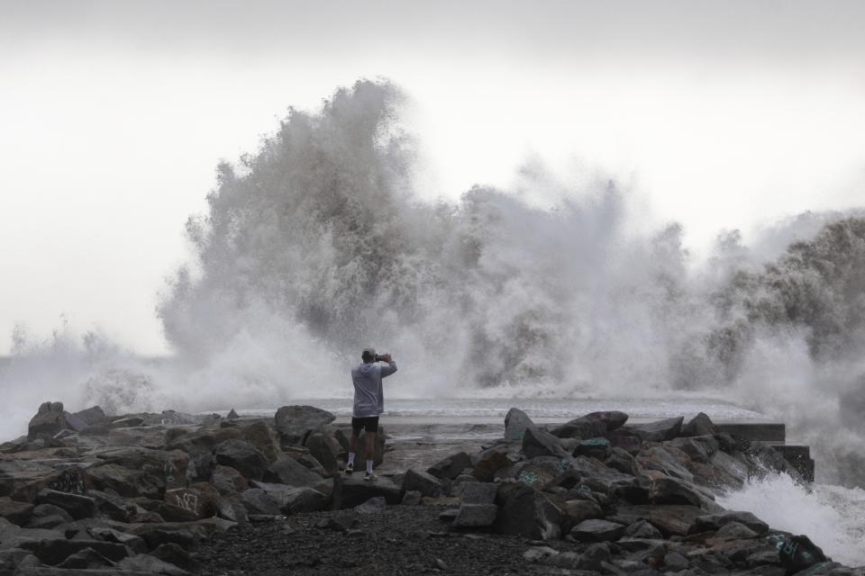 A man takes a snapshot of the waves hitting the breakwater in Barcelona, Spain, Wednesday, Jan. 22, 2020. Massive waves and gale-force winds smashed into seafront towns, damaging many shops and restaurants and flooding some streets. (AP Photo/Joan Mateu)