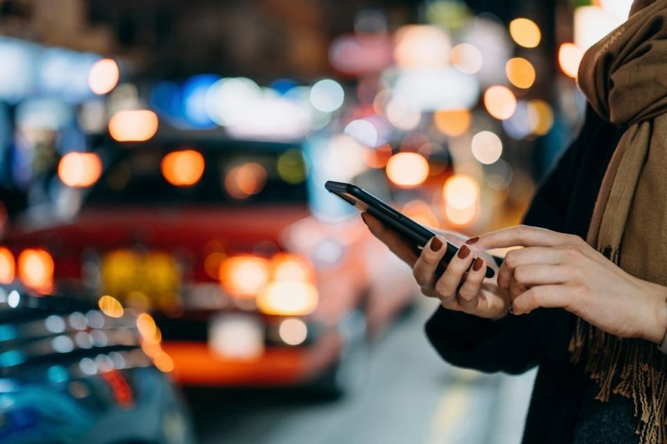 Woman using smart phone in front of busy city street at night