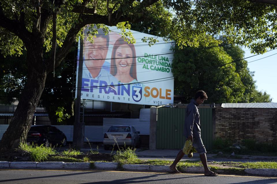 Luis Servin, an unemployed municipality worker who now sells banana and lemons, walks past a billboard promoting presidential candidate Efrain Alegre and running mate Soledad Nunez, in Asuncion, Paraguay, Friday, April 21, 2023. The country's general elections are scheduled for April 30th. (AP Photo/Jorge Saenz)