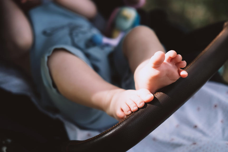 Toddler's bare feet in a stroller, with a focus on safety harness