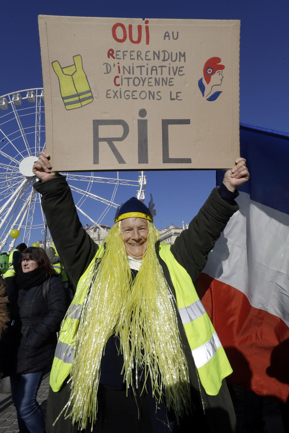 A demonstrator wearing a yellow vest holds a placard reading "Yes at the Referendum of Citizens' Initiatives", during a protest in Marseille, southern France, Saturday, Dec. 29, 2018. The yellow vest movement held several peaceful demonstrations in cities and towns around France, including about 1,500 people who marched through Marseille. (AP Photo/Claude Paris)