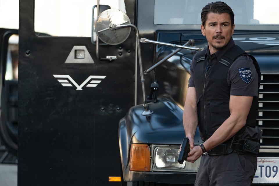 Josh Hartnett standing next to a truck while holding a gun