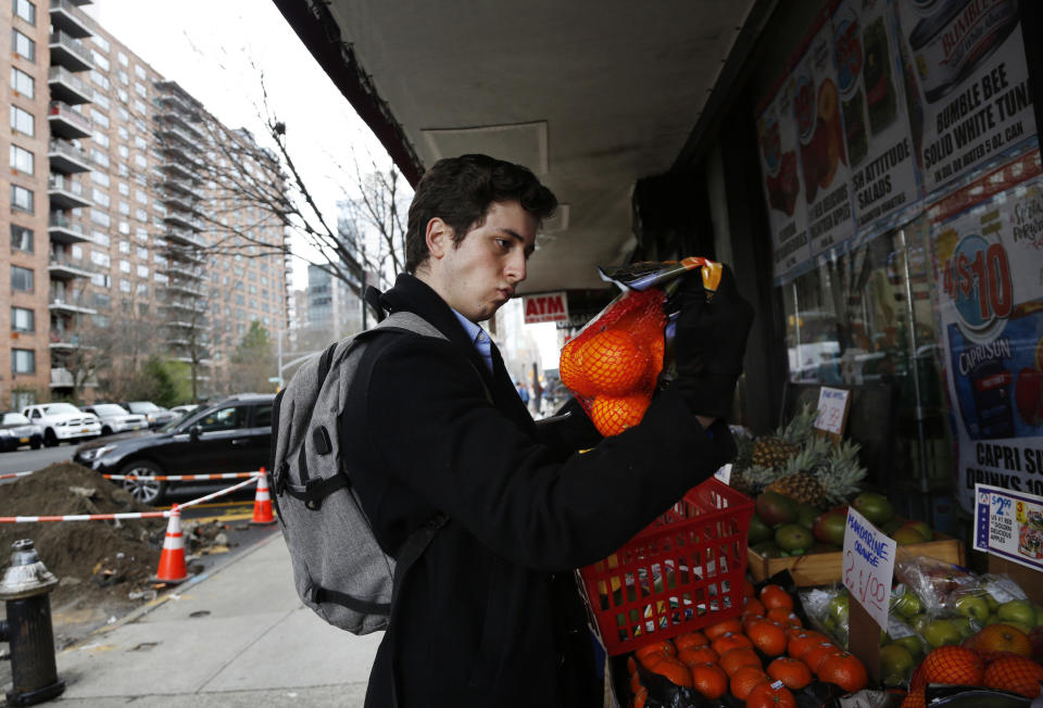 In this March 17, 2020, photo, Liam Elkind, 20, selects a bag of oranges at the Associated Supermarket for 83-year-old Carol Sterling, who is self-quarantined in her apartment in New York due to the coronavirus outbreak. Elkind, a junior at Yale, and his friend, Simone Policano, amassed 1,300 volunteers in 72 hours to deliver groceries and medicine to older New Yorkers and others most vulnerable since the virus swept the city. They call themselves Invisible Hands, and they do something else in the process, provide some human contact and comfort, at a safe distance, of course. (AP Photo/Jessie Wardarski)