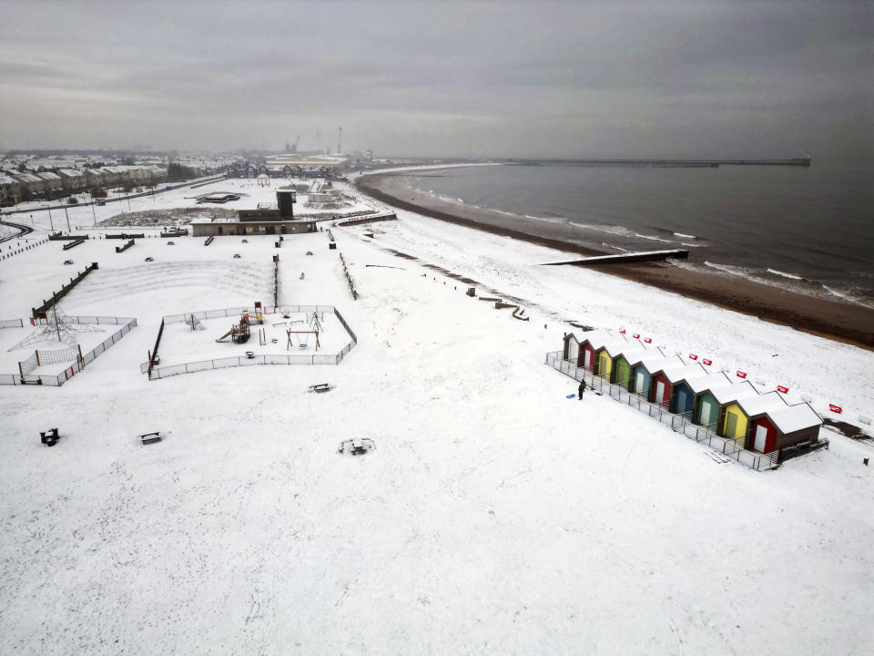 People walk through the snow beside the beach huts at Blyth in Northumberland, England, Sunday, Dec. 3, 2023 as temperatures are tipped to plunge to as low as minus 11C (12.2 F) in parts of the UK over the weekend. (Owen Humphreys/PA via AP)