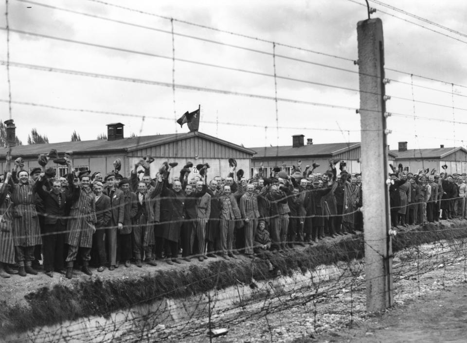 Prisoners behind the electric fence at the Dachau concentration camp on May 3, 1945, cheer the U.S. troops who liberated the camp. Some of the prisoners are wearing striped prison uniforms.