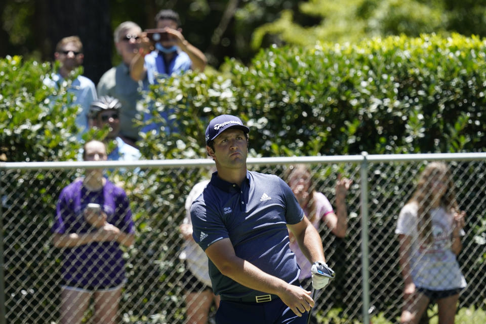 Fans stand behind a fence as Jon Rahm, of Spain, watches his tee shot on the second hole during the first round of the Charles Schwab Challenge golf tournament at the Colonial Country Club in Fort Worth, Texas, Thursday, June 11, 2020. (AP Photo/David J. Phillip)