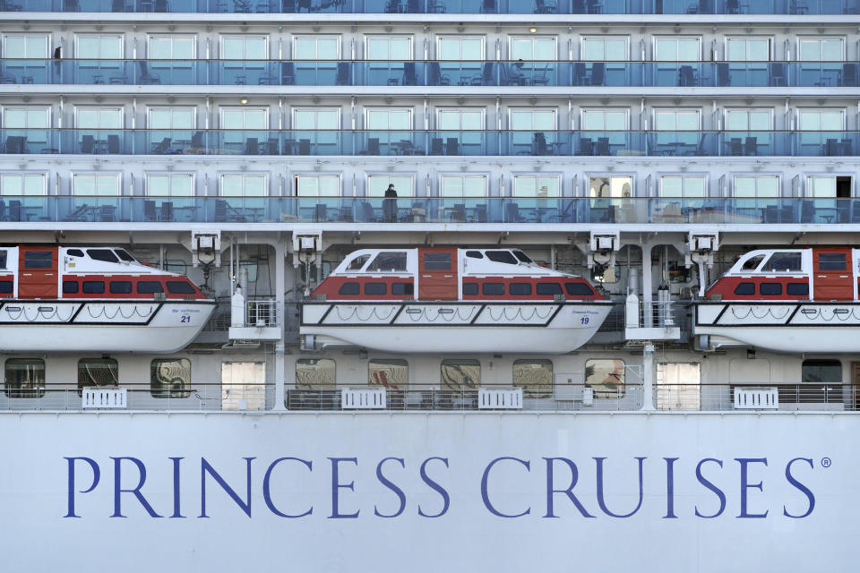 In this Feb. 9, 2020, photo, a passenger stands at the balcony of the cruise ship Diamond Princess anchored off the Yokohama Port in Yokohama, near Tokyo. Japan’s health ministry said Monday, Feb. 10 about 60 more people on the quarantined cruise ship have tested positive for a new virus. (AP Photo/Eugene Hoshiko)