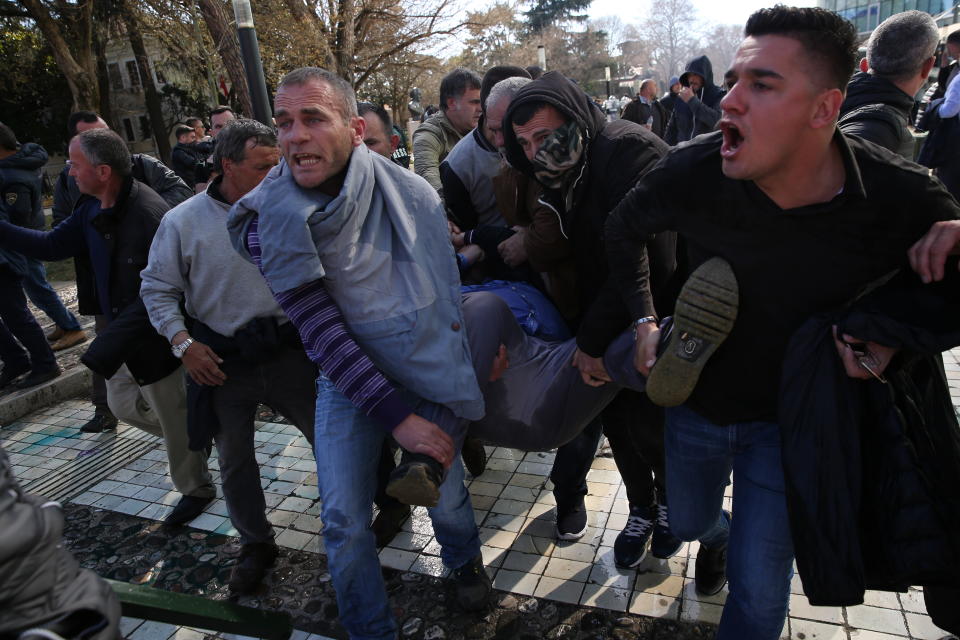 Protesters carry a wounded person as riot police throw shock bombs and tear gas at stone throwing protesters in Tirana, Albania on Saturday, March 16, 2019. Albanian opposition supporters clashed with police while trying to storm the parliament building Saturday in a protest against the government which they accuse of being corrupt and linked to organized crime.(AP Photo/Visar Kryeziu)