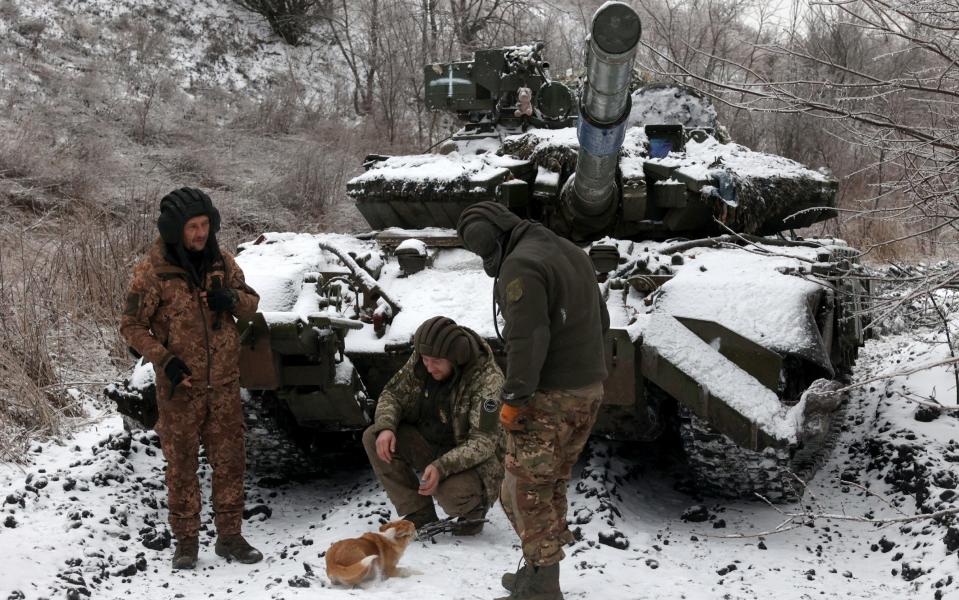 Ukrainian soldiers play with a dog next to a tank, on positions near to the town of Bakhmut