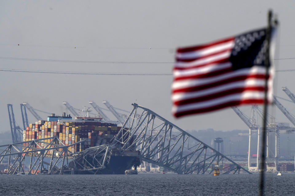 An American flag flies on a moored boat as the container ship Dali rests against wreckage of the Francis Scott Key Bridge, Tuesday, March 26, 2024, as seen from Pasadena, Md. (AP Photo/Mark Schiefelbein)