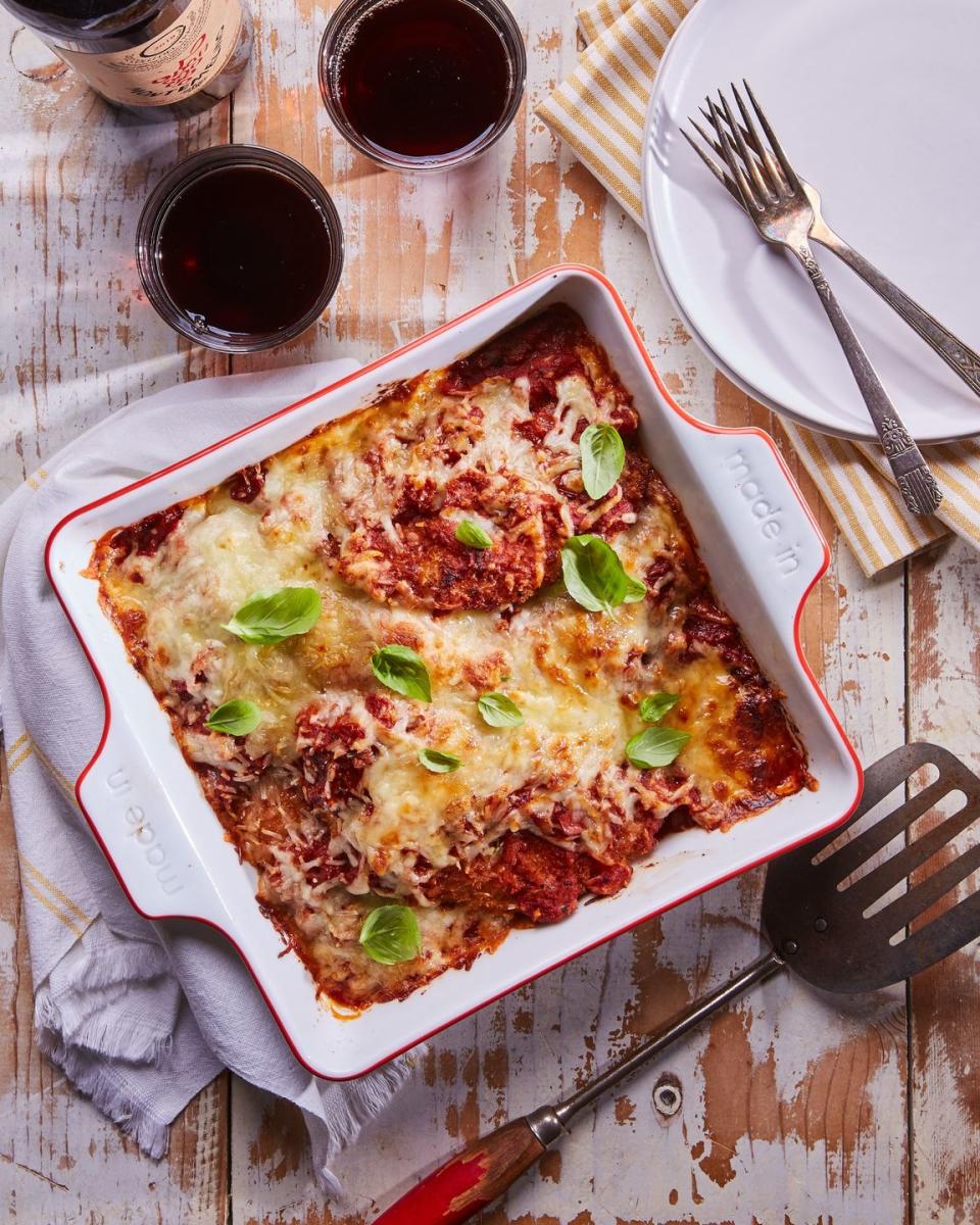 crispy chicken parmesan baked in a white square baking dish with melted cheese and fresh basil leaves on top