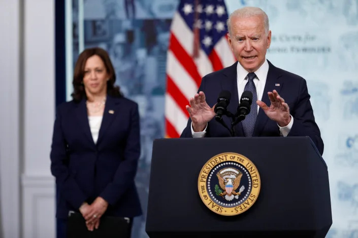 President Biden speaks at a podium bearing the Presidential Seal in front of Kamala Harris, who stands next to an American flag.