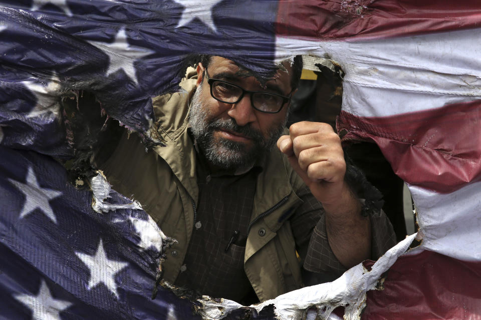 FILE - In this May 11, 2018 file photo, an Iranian protestor clenches his fist behind a burnt representation of the U.S. flag during a protest over U.S. President Donald Trump's decision to pull out of the nuclear deal with world powers, in Tehran, Iran. Ahead of the 40th anniversary of Iran’s Islamic Revolution, the country’s government is allowing more criticism to bubble up to the surface. But limits still clearly exist in Iran’s Shiite theocracy and the frustration people feel may not be satiated by complaining alone. (AP Photo/Vahid Salemi, File)