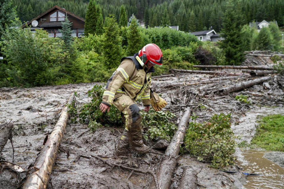 A rescue worker climbs over tree trunks after a mudslide has hit several residential buildings in Bagn in Valdres, Norway, Tuesday, Aug. 8, 2023. Officials in northern Europe are warning people to stay inside as stormy weather batters the region. Storm Hans has cancelled ferries, delayed flights, flooded streets and injured people. Norwegian authorities expected “extremely heavy rainfall” on Tuesday. (Cornelius Poppe/NTB Scanpix via AP)