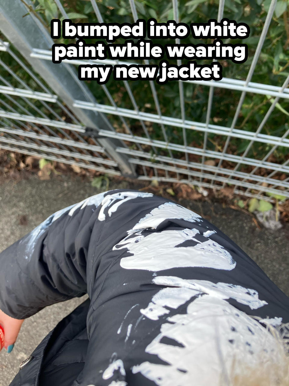 A person's new jacket splattered with white paint against a metal fence backdrop