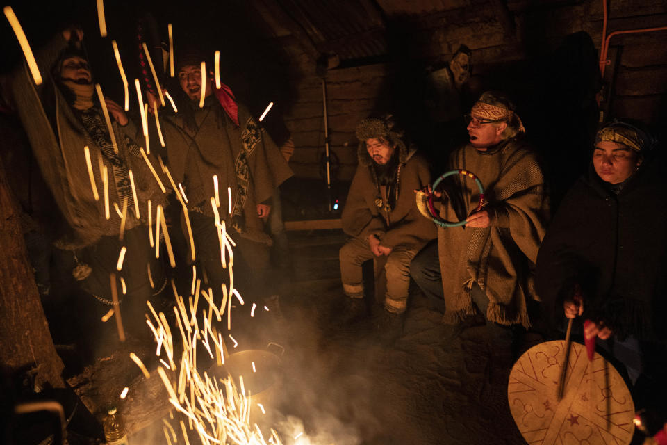 Mapuche community members sing around a campfire as one holds a trutruka horn and another beats a ceremonial drum known as a kultrun inside a ruka, a traditional thatch-roofed rural dwelling, in the culmination of We Tripantu, the Mapuche new year, in Carimallin, southern Chile, on Sunday, June 26, 2022. (AP Photo/Rodrigo Abd)