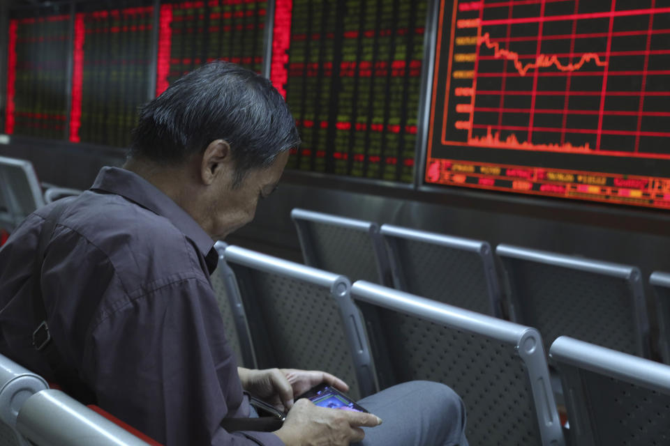 In this Wednesday, Sept. 25, 2019, photo, a Chinese man plays a game on his mobile phone as he monitors stock prices at a brokerage in Beijing. Asian stock markets followed Wall Street higher Thursday, Sept. 26, 2019, after U.S. President Donald Trump suggested a costly tariff war with China could be resolved soon. (AP Photo/Ng Han Guan)