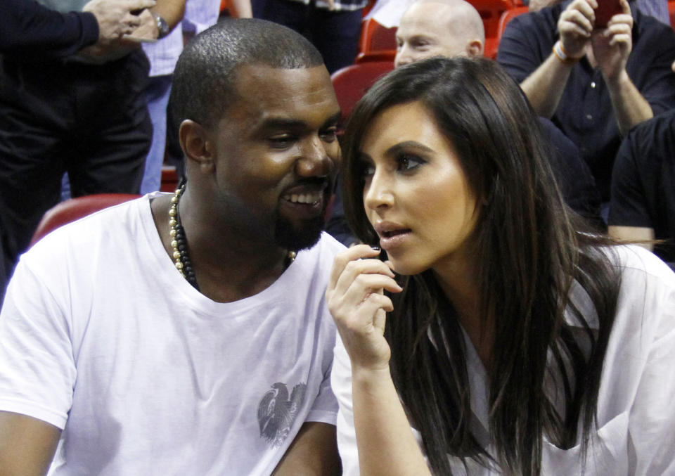 FILE - This Dec. 6, 2012 file photo shows singer Kanye West, left, talks to his girlfriend Kim Kardashian before an NBA basketball game between the Miami Heat and the New York Knicks in Miami. As the tabloids speculated over whether or not Jessica Simpson was expecting her second baby and the media zeroed in on Kate Middleton's pregnancy, Kardashian admits it was nice to be away from the glare of the spotlight as she was in the early stages of her own pregnancy. Now that the word is out, 32-year-old Kardashian says her motherly instincts have made her pull back from being so open about her personal life. (AP Photo/Alan Diaz, file)