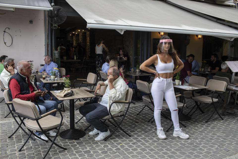 A cafe-restaurant staff stands outside a shop as people drink coffee in Monastiraki district of Athens, on Monday, May 25, 2020. Greece restarted regular ferry services to its islands Monday, and cafes and restaurants were also back open for business as the country accelerated efforts to salvage its tourism season. (AP Photo/Petros Giannakouris)