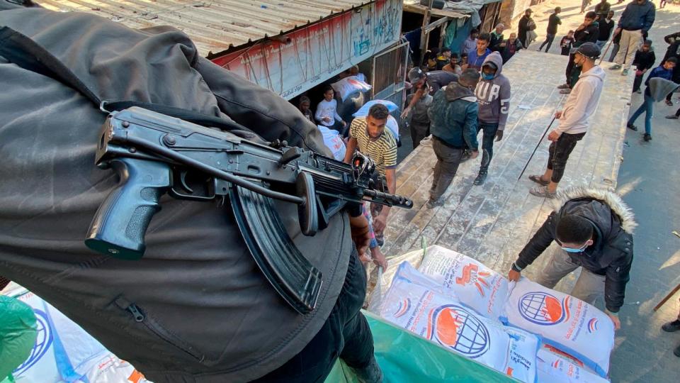 PHOTO: Palestinians unload wheat sacks from a humanitarian aid truck into a grocery store under guard by Hamas fighters in Rafah, Gaza Strip, Dec. 19, 2023. (AP)