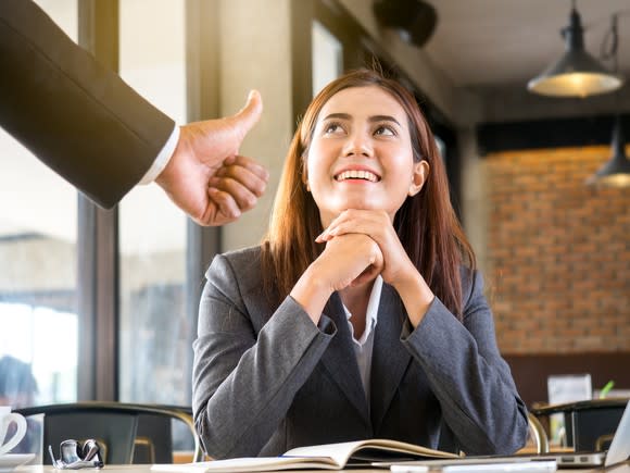 Man giving a thumbs up to a business woman sitting at a desk