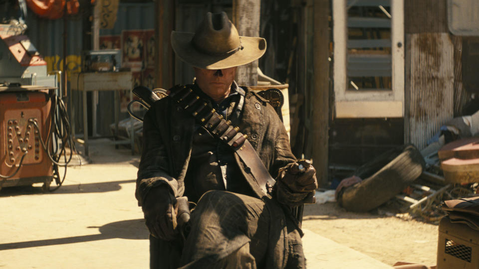 The Ghoul sits slumped in a chair with his cowboy hat lowered over his face in the Fallout TV show