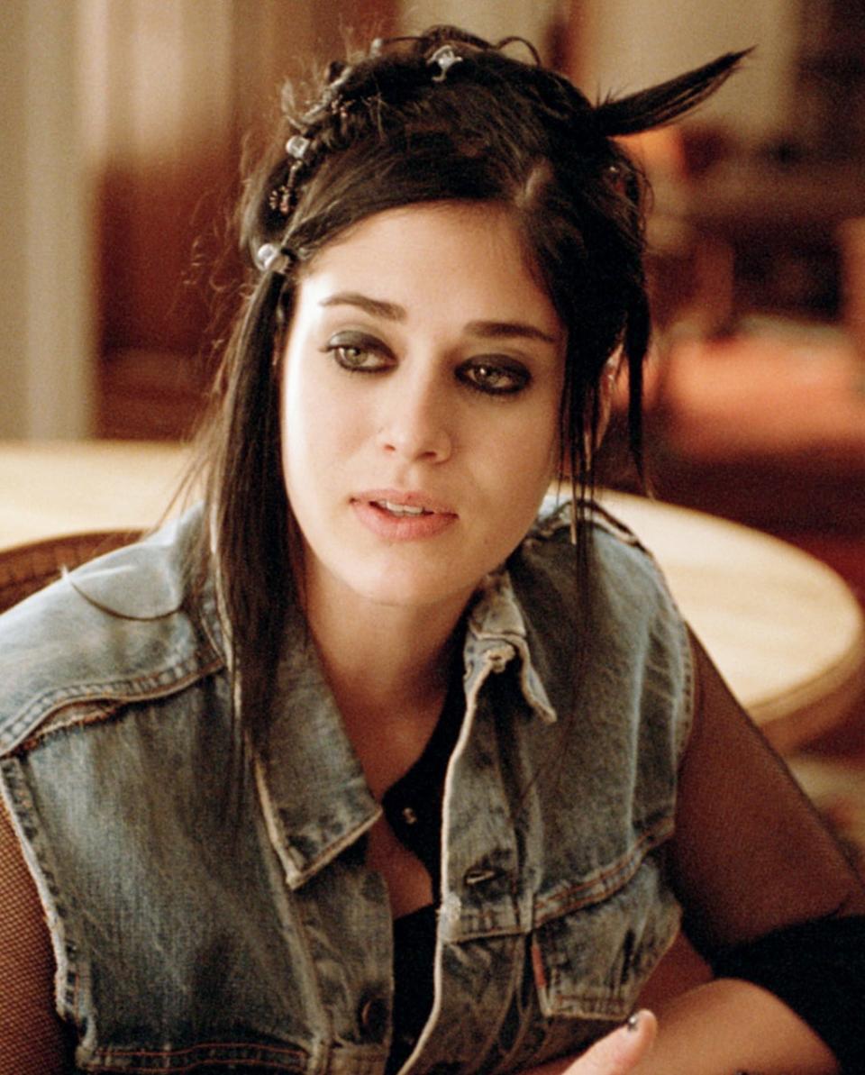 closeup of her with dark eye makeup and a denim vest