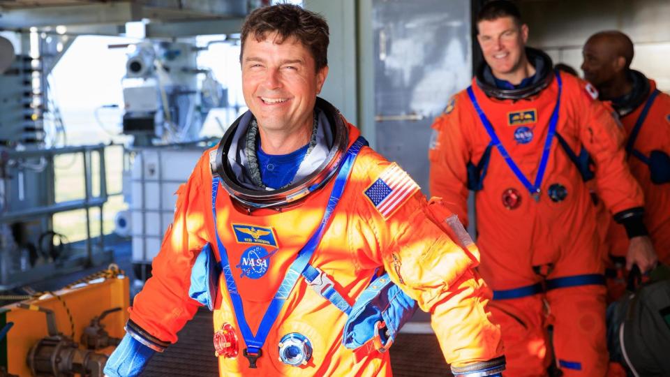 three astronauts walking in a row with the first astronaut in front, reid wiseman, smiling