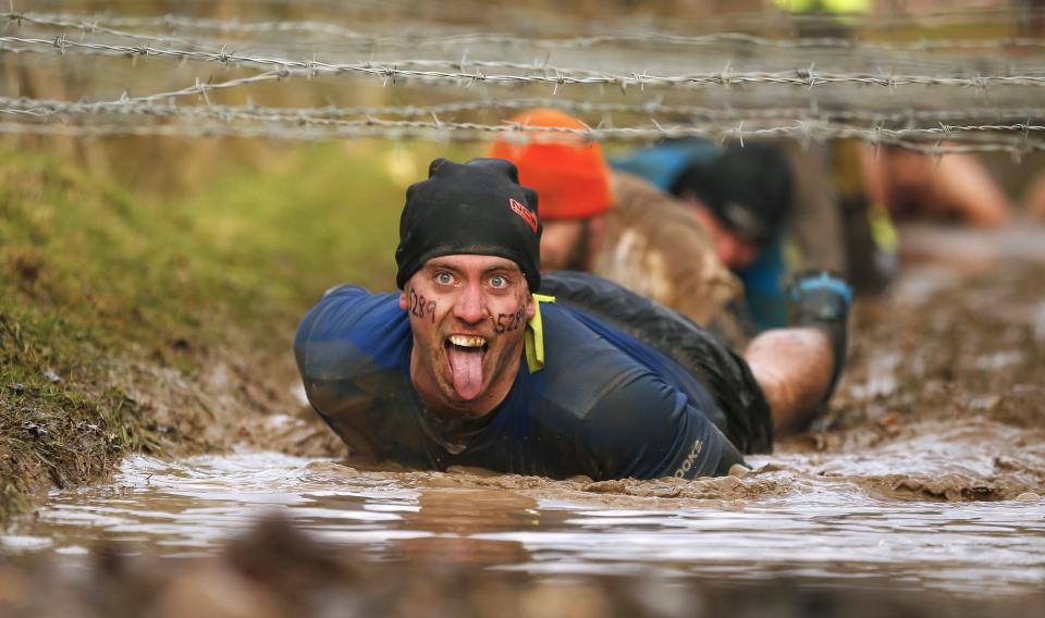 A competitor gestures as he crawls beneath barbed wire during the Tough Guy event in Perton, central England