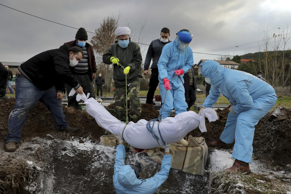 Volunteers and relatives wearing protective clothing and masks lower the body of Ghorbanali Mahmoudi, 59, who died from COVID-19 into a grave at a cemetery in the Haji Kola village on the outskirts of the city of Ghaemshahr, in northern Iran, Saturday, Dec. 19, 2020. (AP Photo/Ebrahim Noroozi)