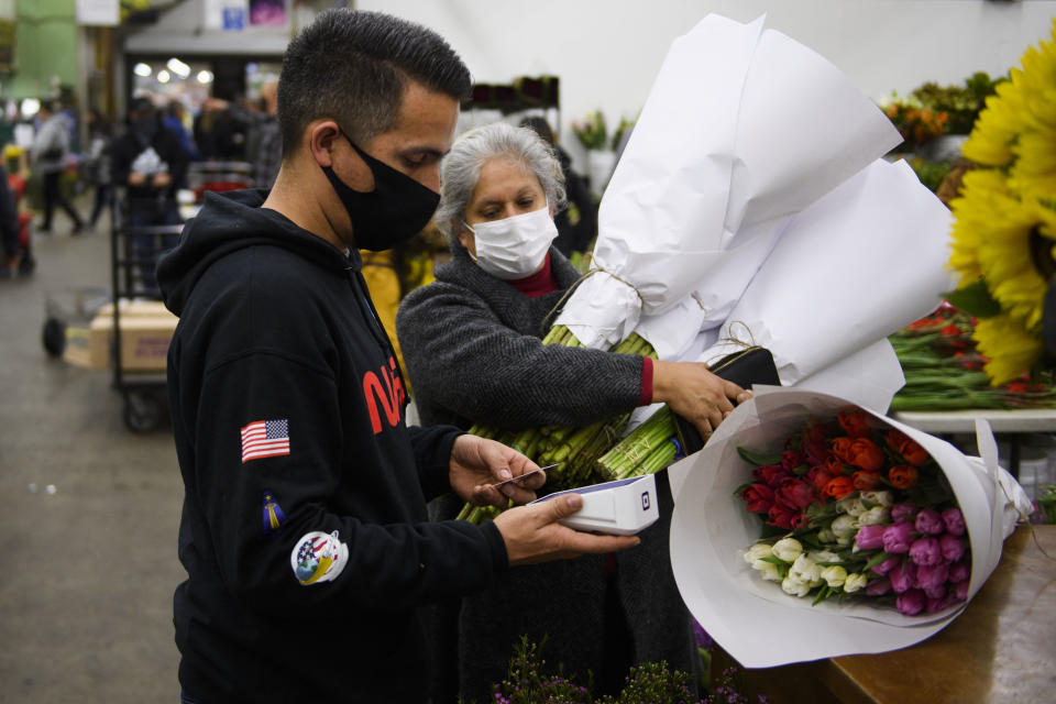 Jorge Olivera (L) of Stems Floral uses a Square Inc. credit card reader for a customer as they buy flowers ahead of the Valentine's Day holiday at the Southern California Flower Market on February 12, 2021 in Los Angeles, California. - While some florists note an increased demand for socially distant gifts, the Covid-19 pandemic has impacted global supply chains and shut down most large events including weddings where flowers are popular. The Valentine's Day and Mother's Day holidays are historically the two busiest days of the year for floral businesses. (Photo by Patrick T. FALLON / AFP) (Photo by PATRICK T. FALLON/AFP via Getty Images)